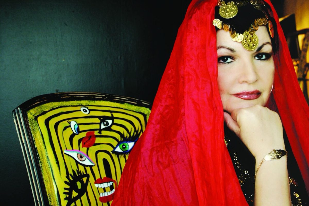 Jihan Jamal in a red silk head veil and gold coin headdress, chin resting on her hand